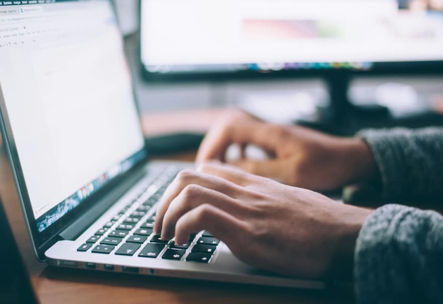 Manos escribiendo en el teclado de un portátil sobre una mesa de trabajo