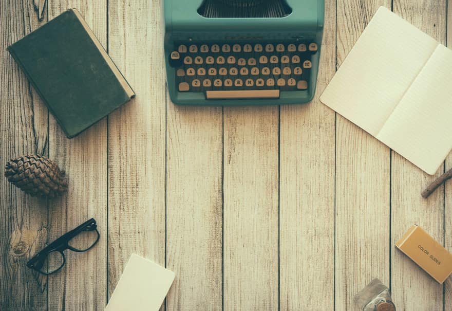Máquina de escribir junto a cuadernos, gafas y lápices sobre una mesa de madera