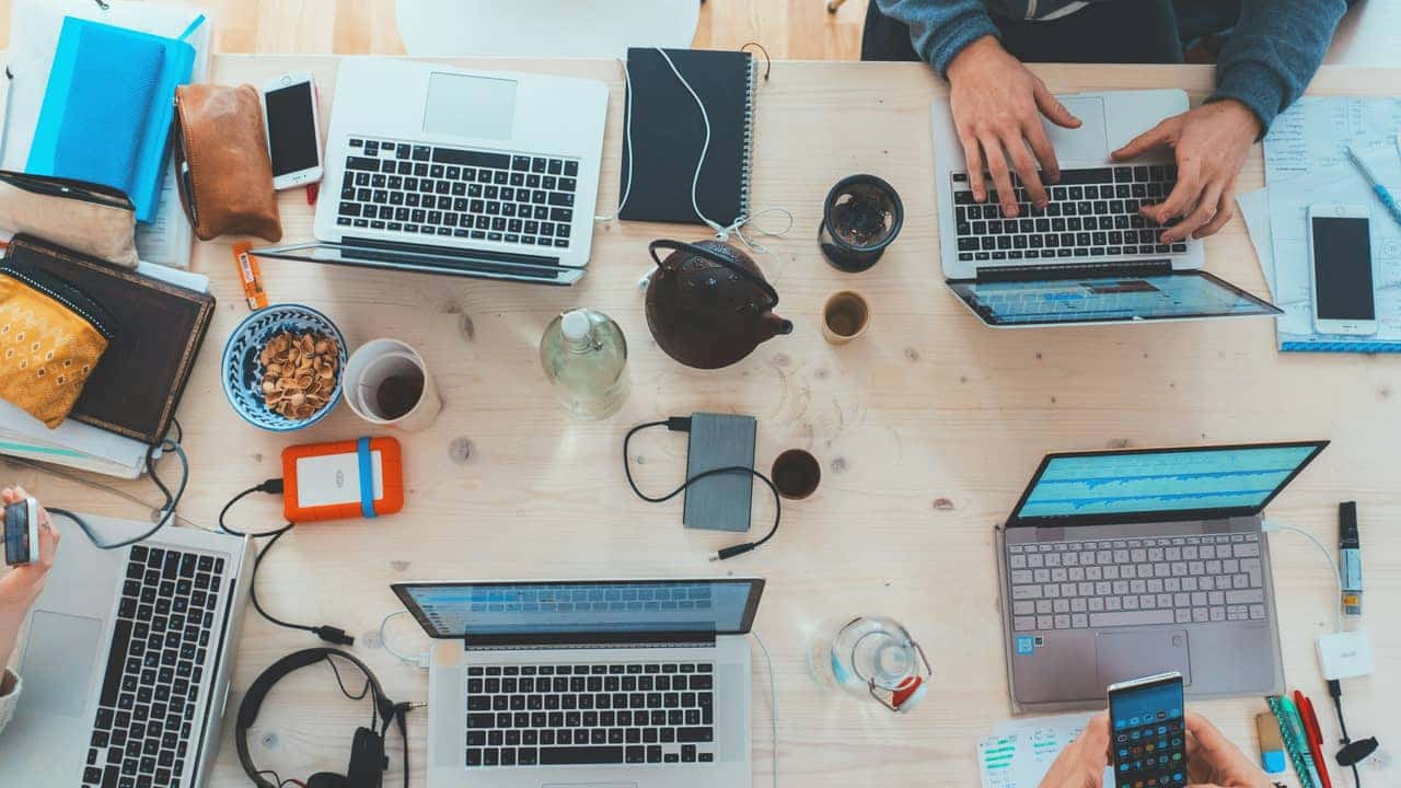 Vista cenital de una mesa de trabajo con varios portátiles y teléfonos móviles